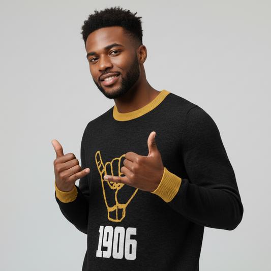 Man wearing a black sweater with gold accents and a logo, giving a thumbs-up gesture on a gray background.